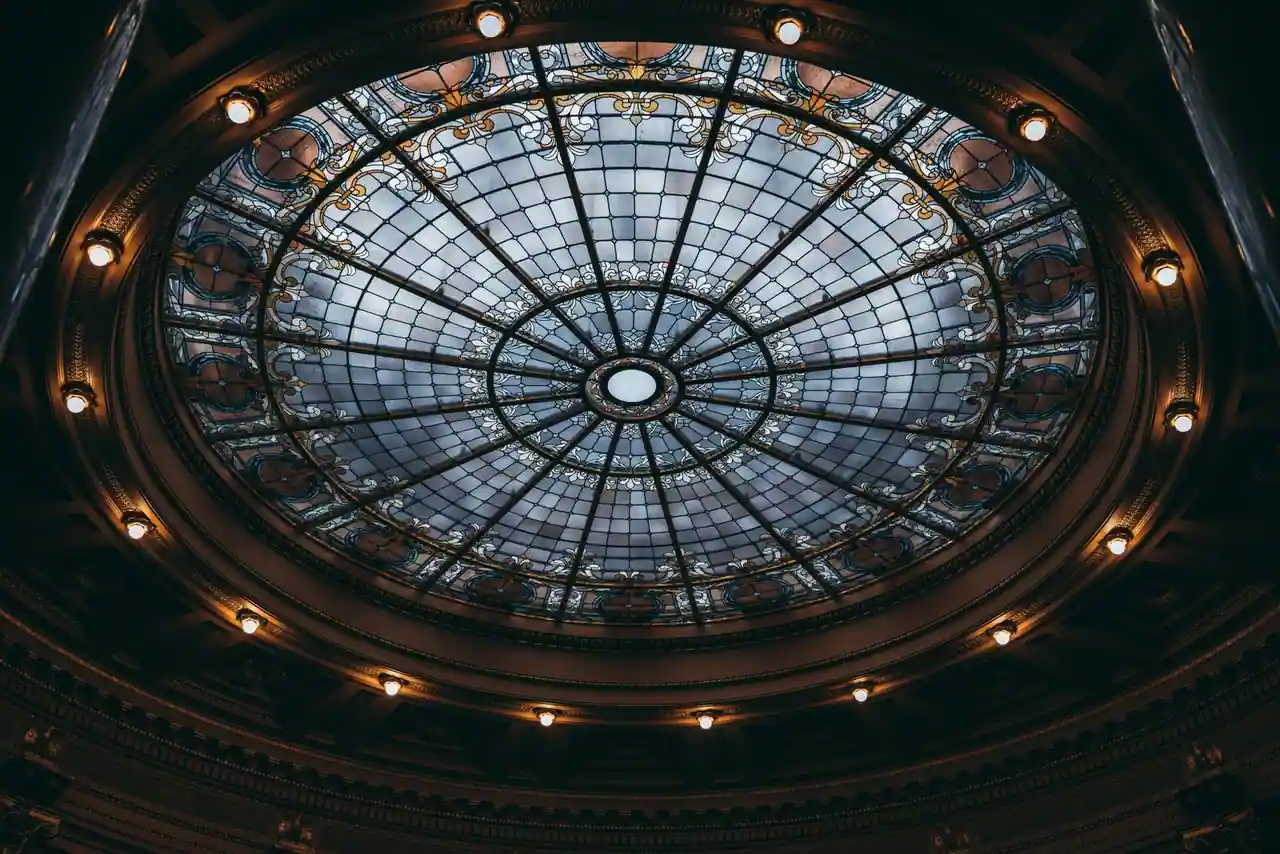 Coupole de verre ornée vue de l’intérieur, baignée de lumière au sommet d’une rotonde.