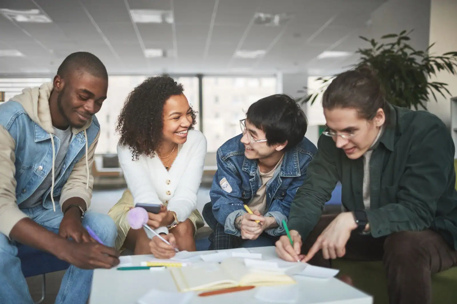 Quatre jeunes assis autour d'une table prennent des notes et échangent en souriant sur un projet commun