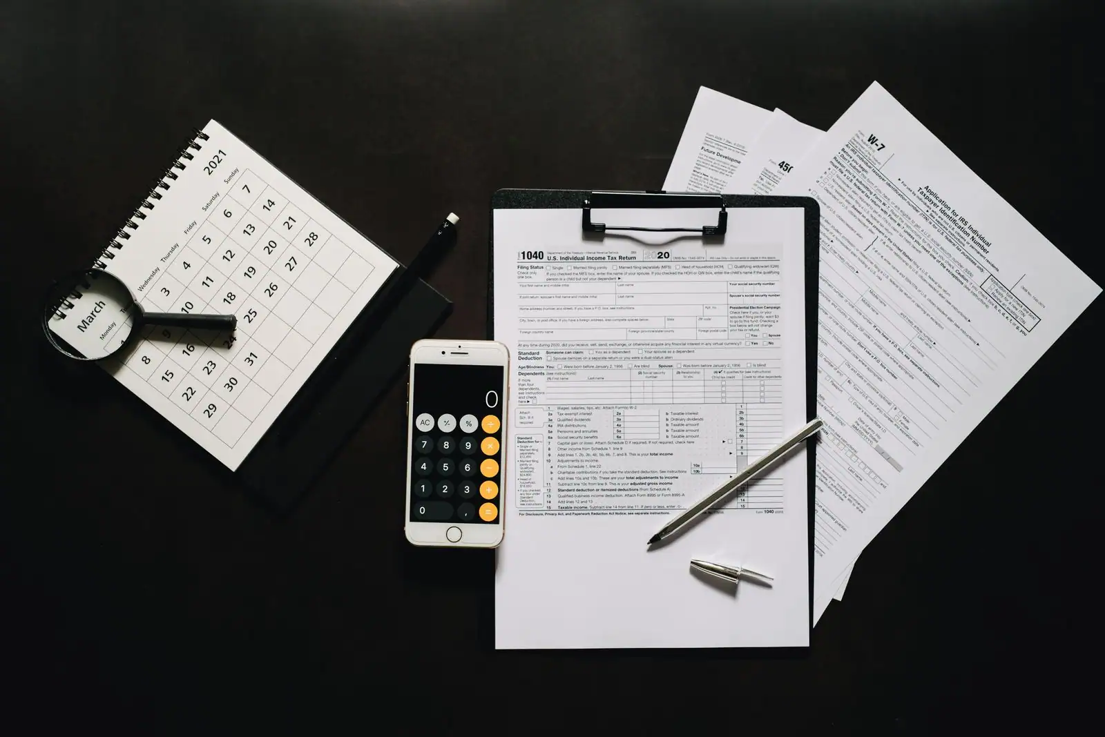 Formulaire de déclaration d'impôt, calculatrice sur smartphone et stylo posés sur un bureau sombre