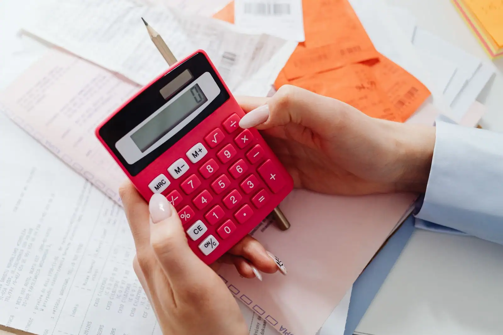 Une personne effectue un calcul sur une calculatrice, au-dessus de reçus et de documents financiers.