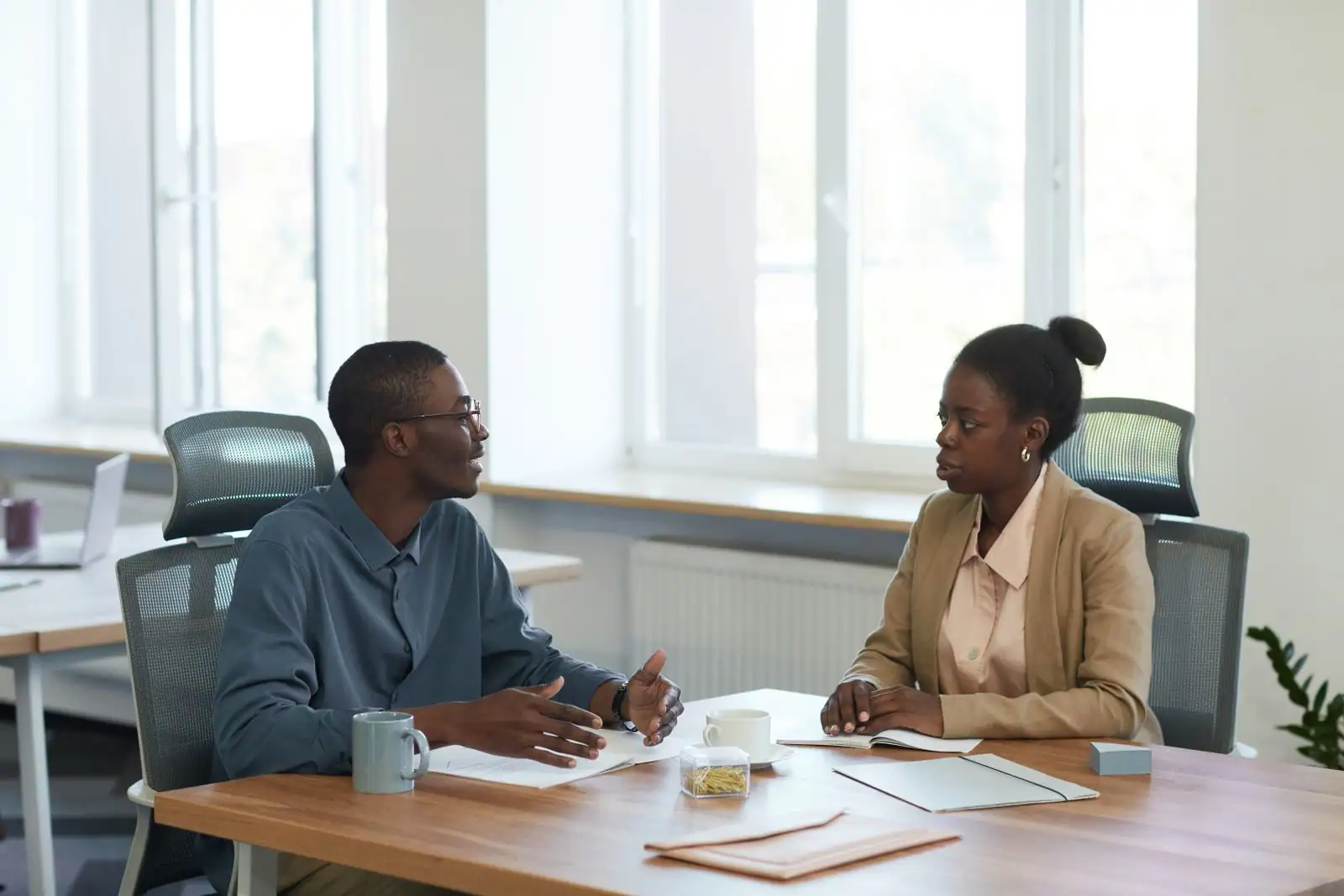 Deux collègues en conversation posée de part et d'autre d'un bureau, dans une attitude d'écoute attentive