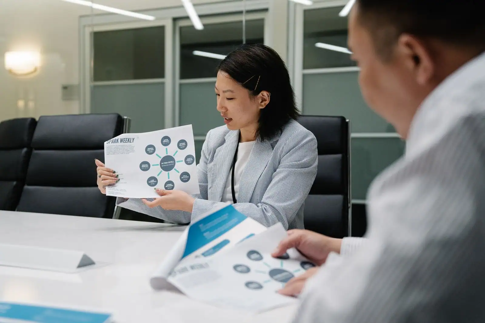 Personne présentant un document à une équipe réunie autour d'une table, en milieu professionnel.