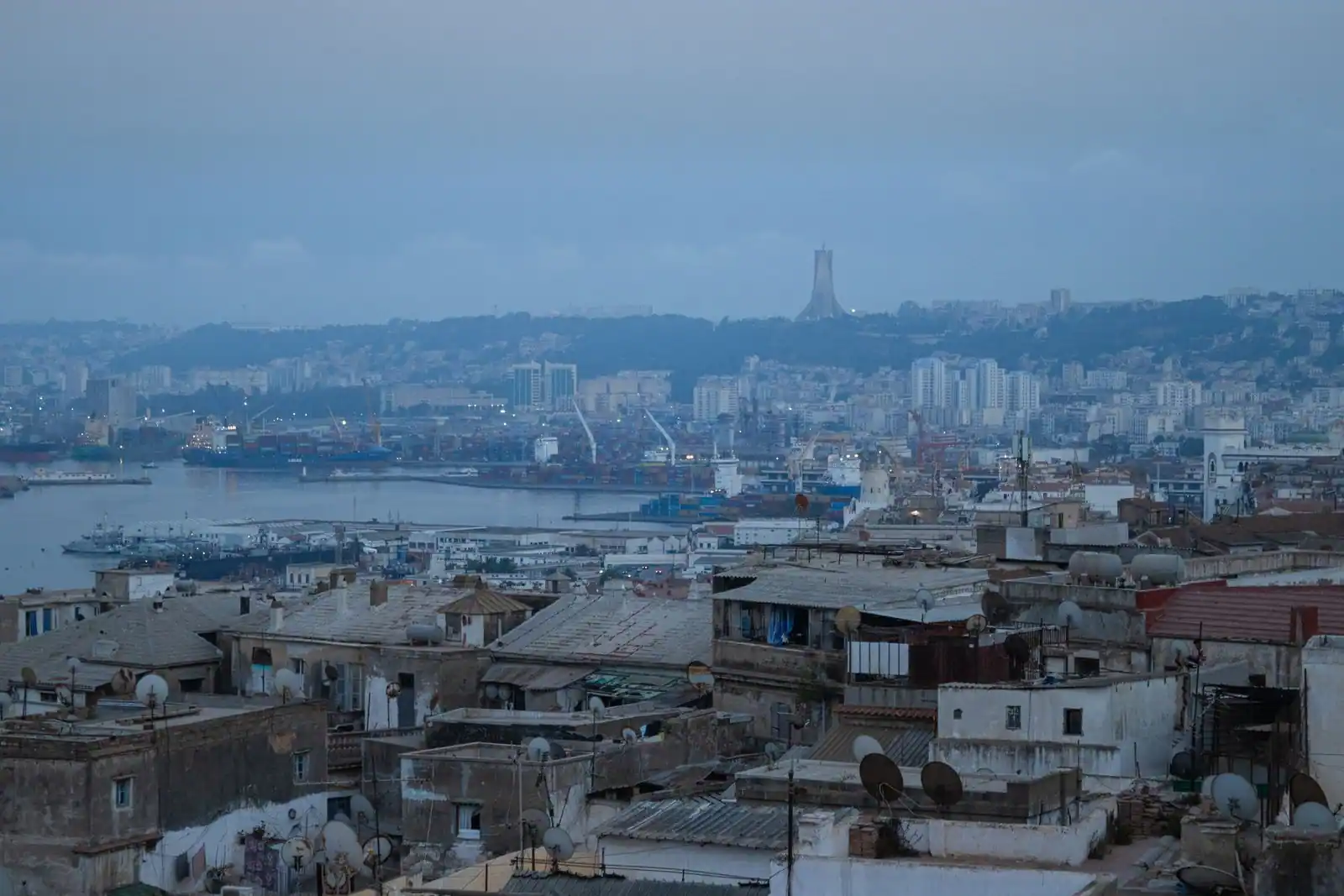 Vue aérienne d'Alger au crépuscule : la baie, le port et le Mémorial du Martyr sur la colline