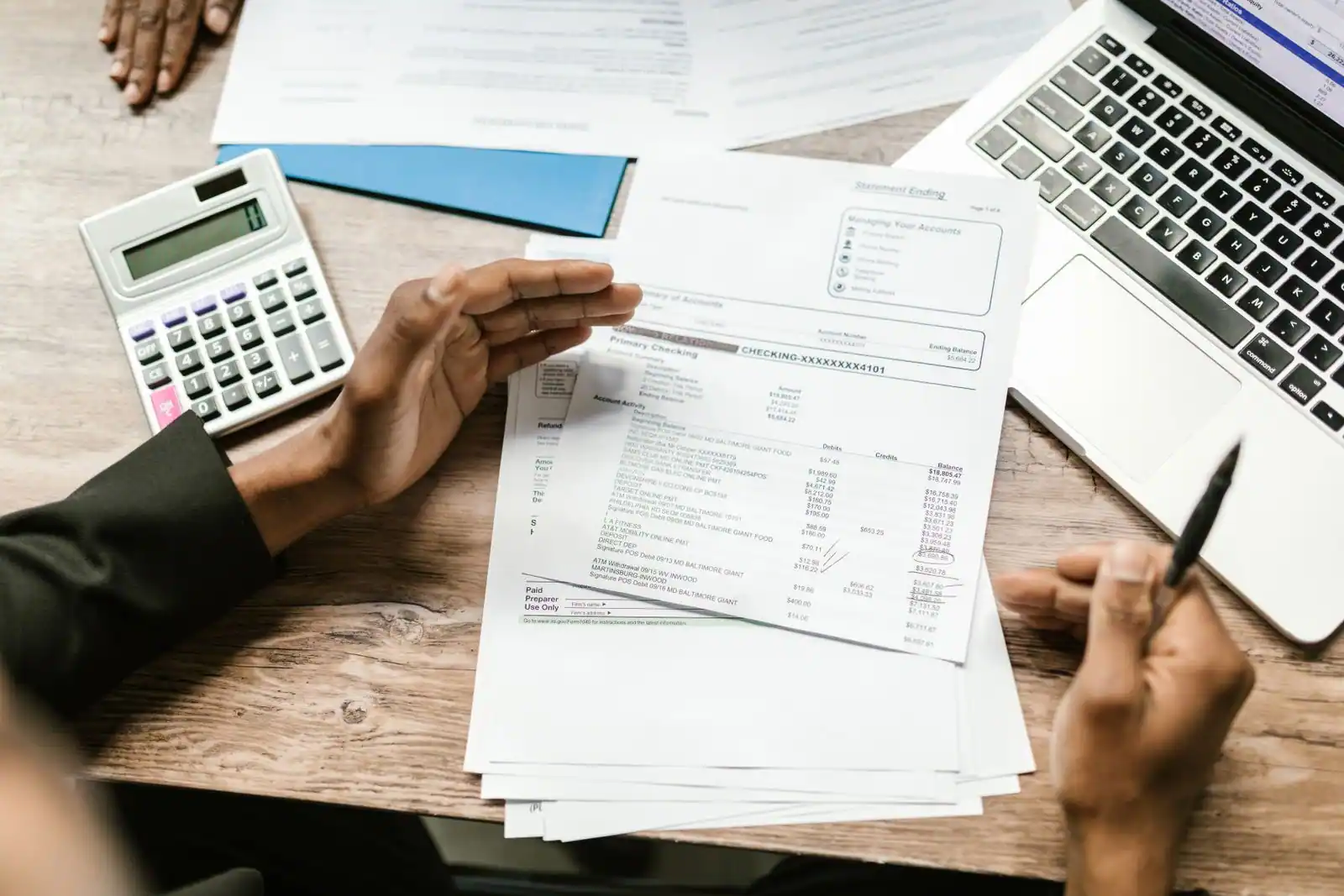 Relevé de compte bancaire examiné à la main près d'une calculatrice et d'un ordinateur portable
