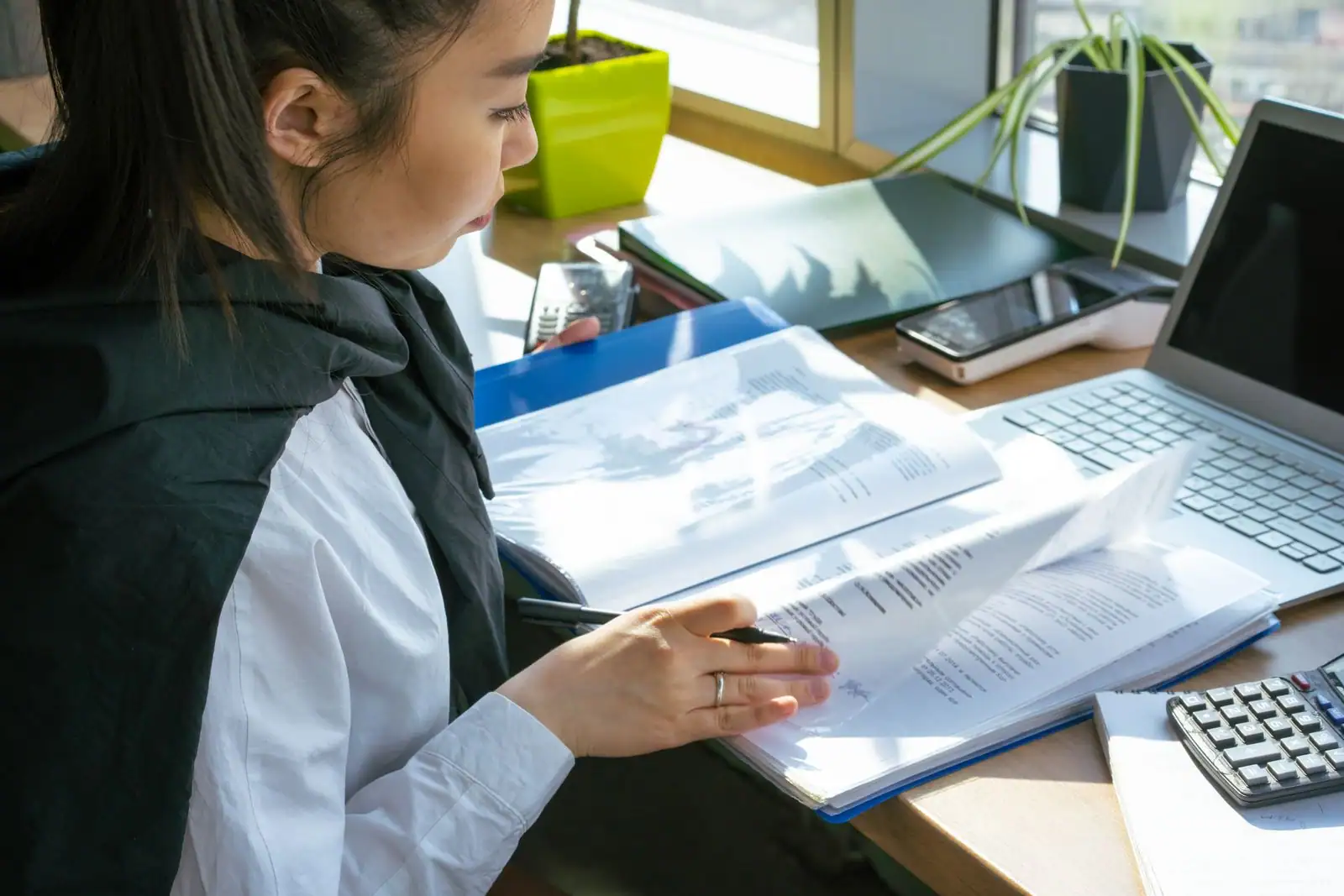 Femme examinant des documents à son bureau, devant un ordinateur portable et un smartphone