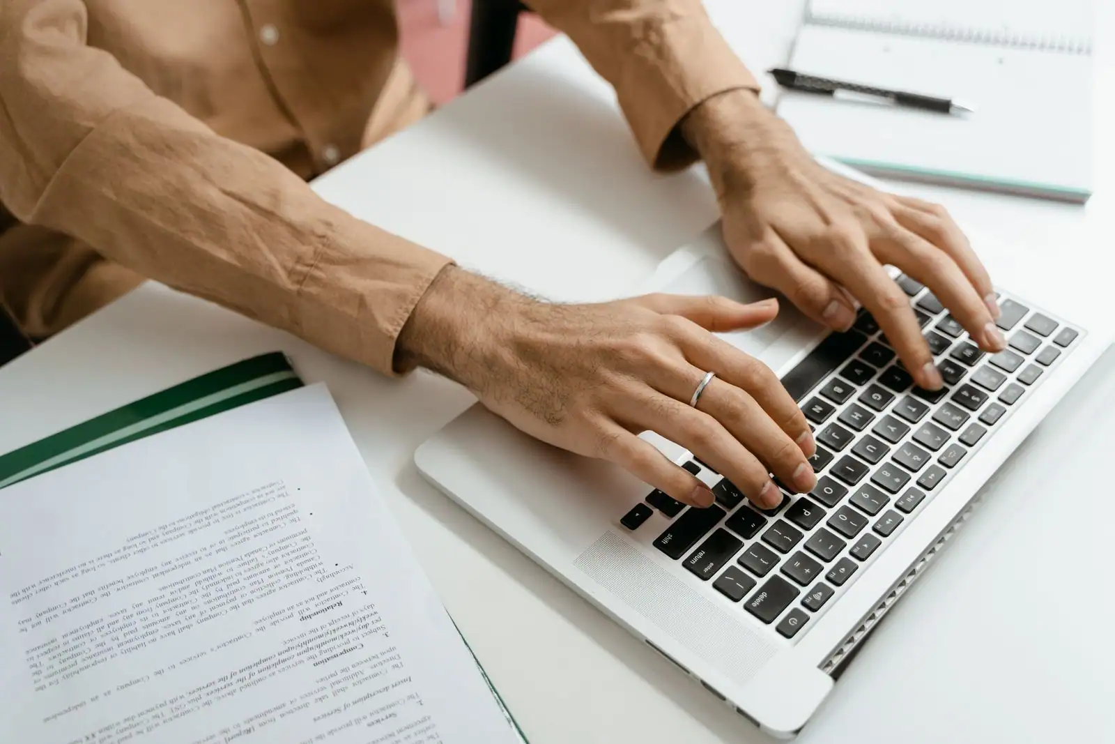 Mains tapant sur le clavier d un ordinateur portable, à côté d un document imprimé sur le bureau