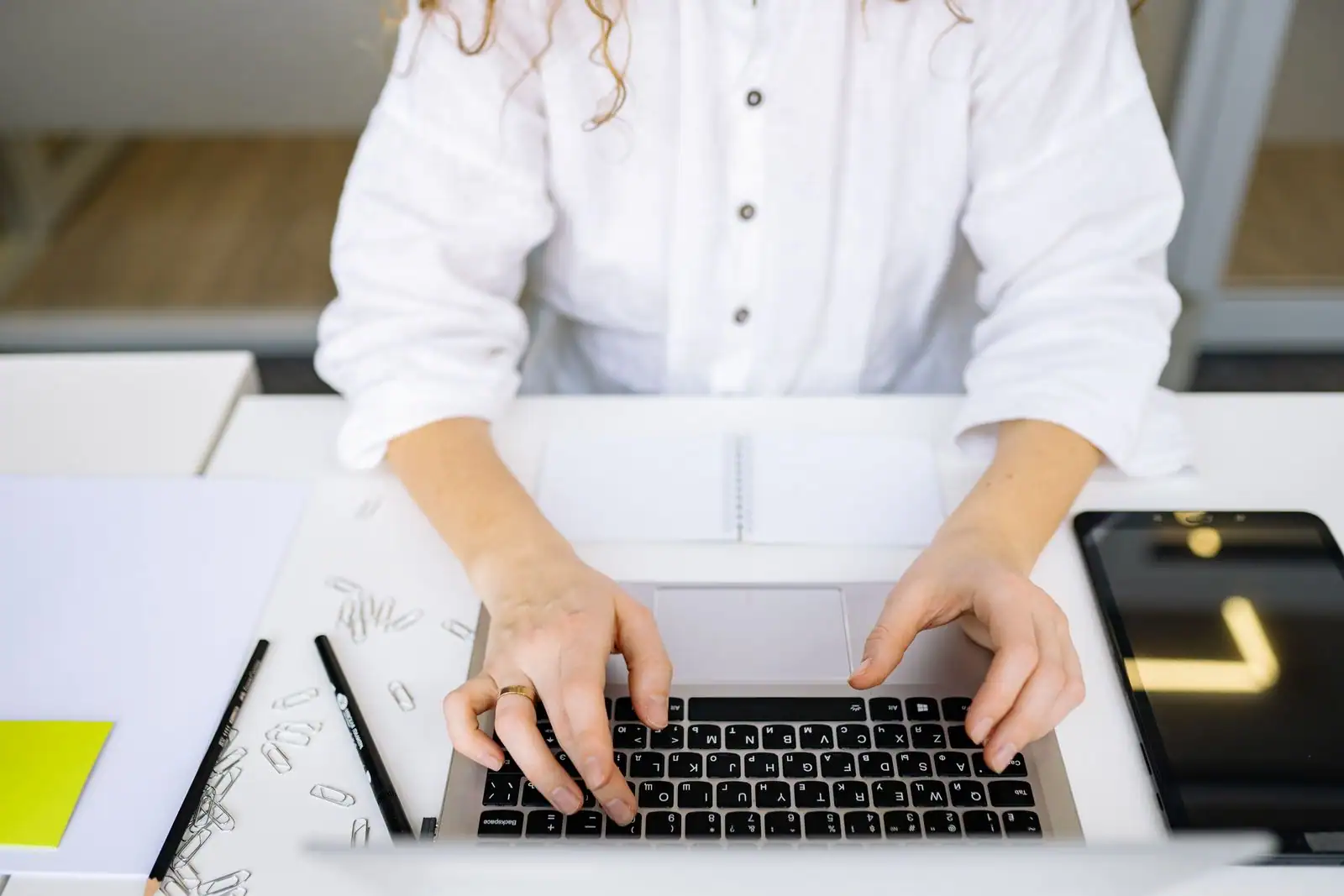 Une personne tape sur le clavier d'un ordinateur portable, vue de dessus, à un bureau clair