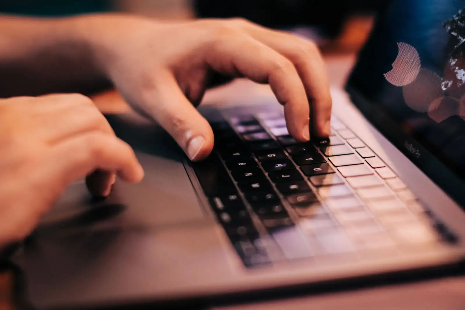 Mains tapant sur le clavier d'un ordinateur portable, en gros plan dans une lumière tamisée