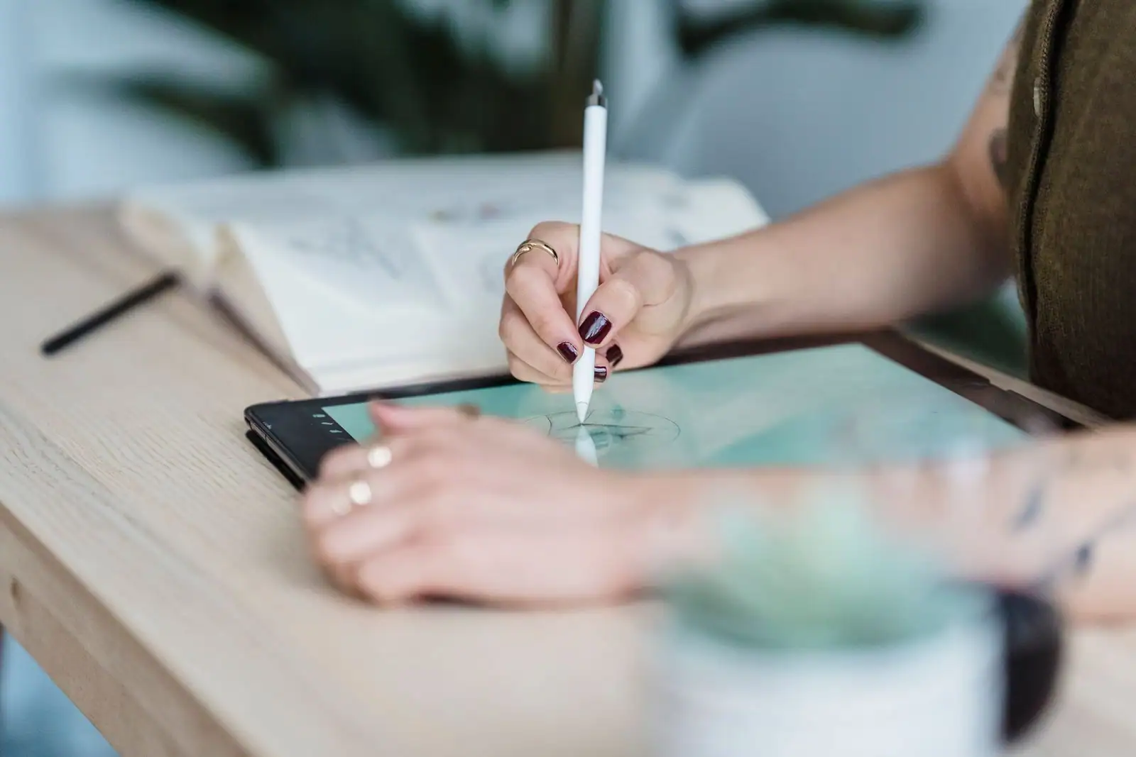 Designer dessinant au stylet sur une tablette graphique, un carnet d'esquisses ouvert à côté sur le bureau