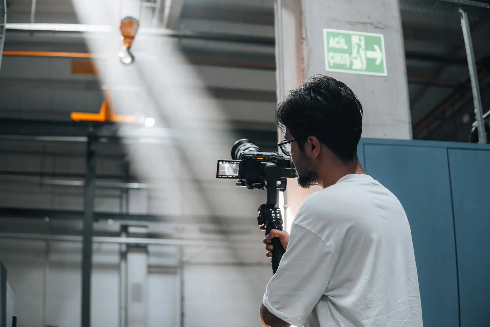 Vidéaste filmant avec une caméra montée sur un stabilisateur, dans un grand espace industriel