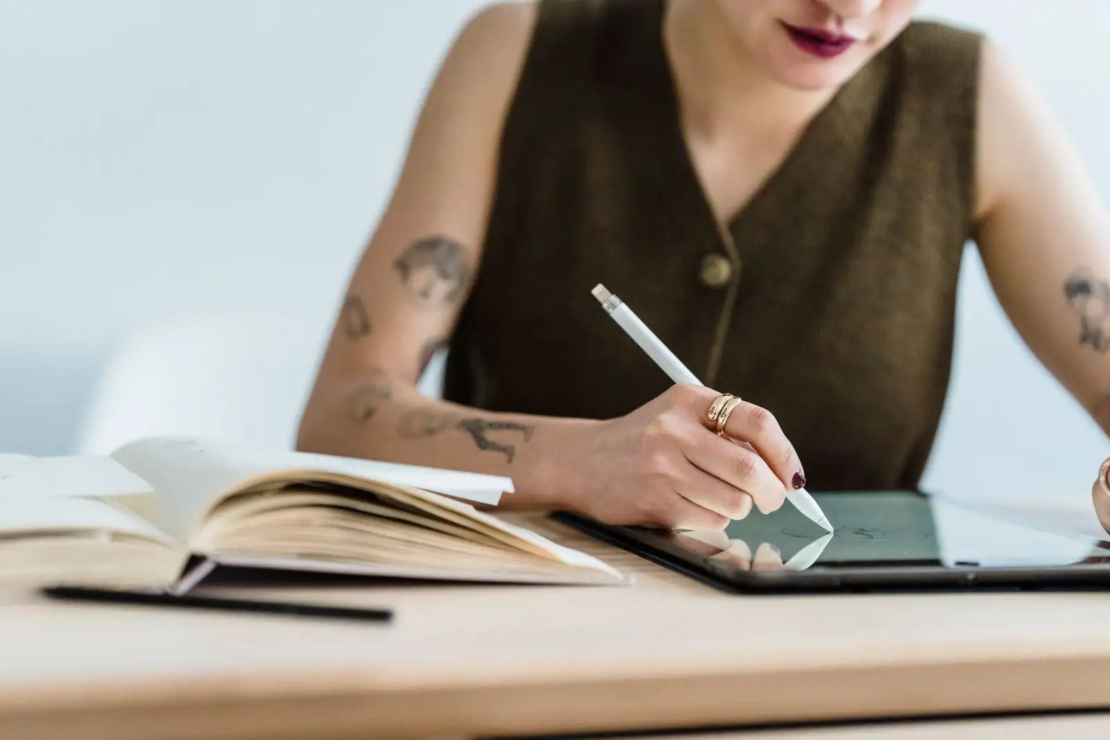 Une graphiste dessine au stylet sur sa tablette, à son bureau, à côté d'un carnet de croquis ouvert.