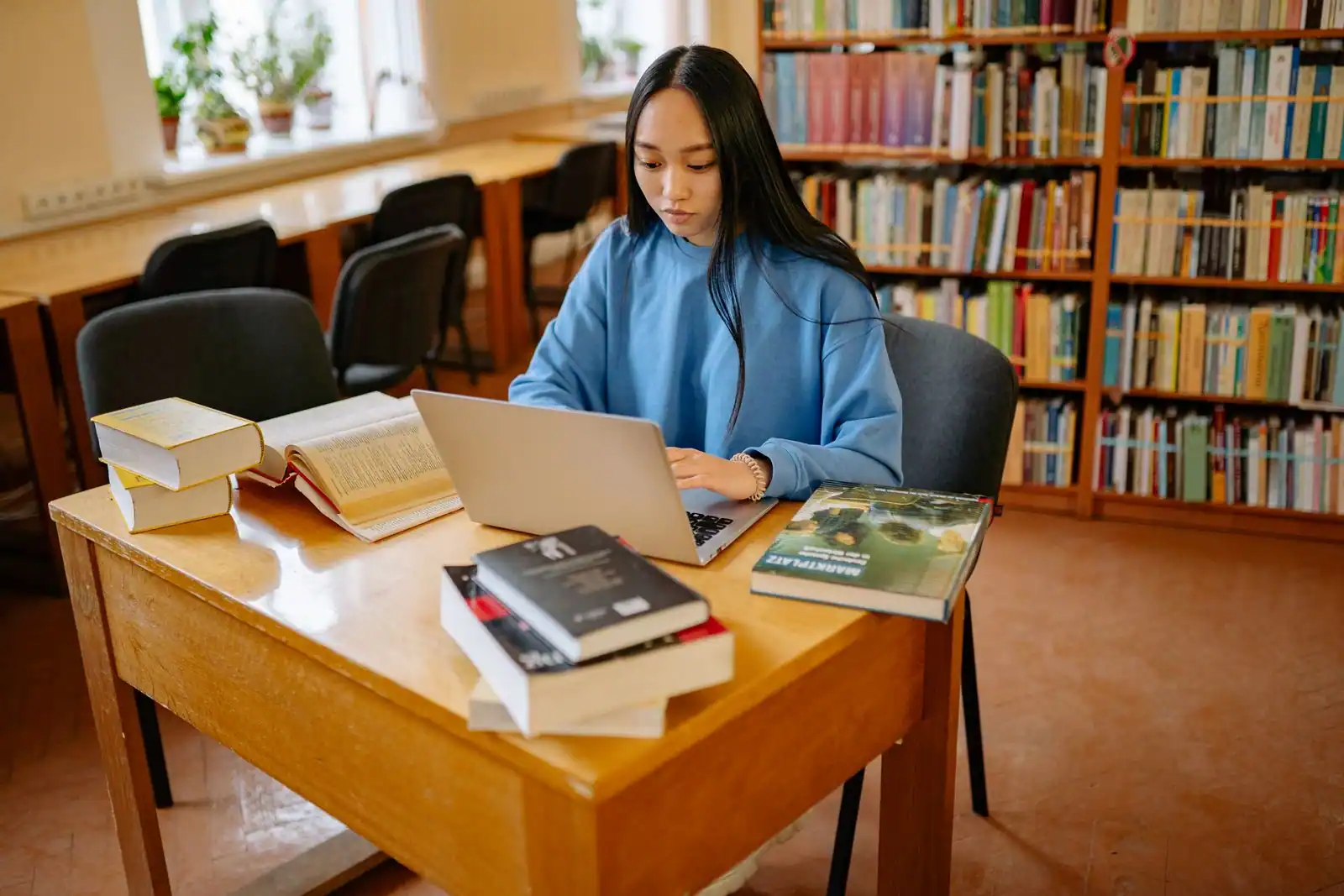 Étudiante concentrée sur un ordinateur portable dans une bibliothèque, entourée de livres