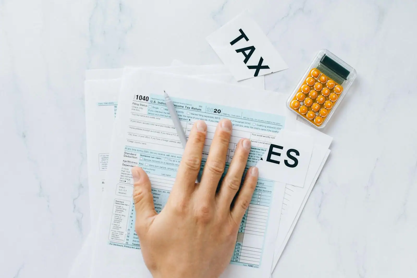 Main posée sur un formulaire de déclaration de revenus, à côté d'une calculatrice et d'un stylo