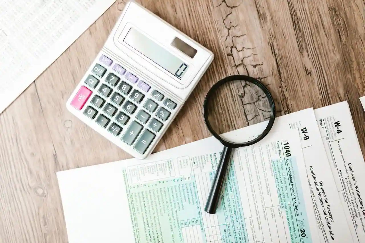 Calculatrice, loupe et formulaires fiscaux posés sur un bureau en bois, évoquant le calcul de l'impôt sur le revenu