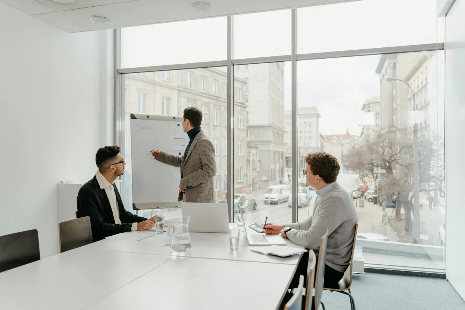 Un manager présente devant un paperboard à deux collègues réunis autour d'une table, dans un bureau lumineux.