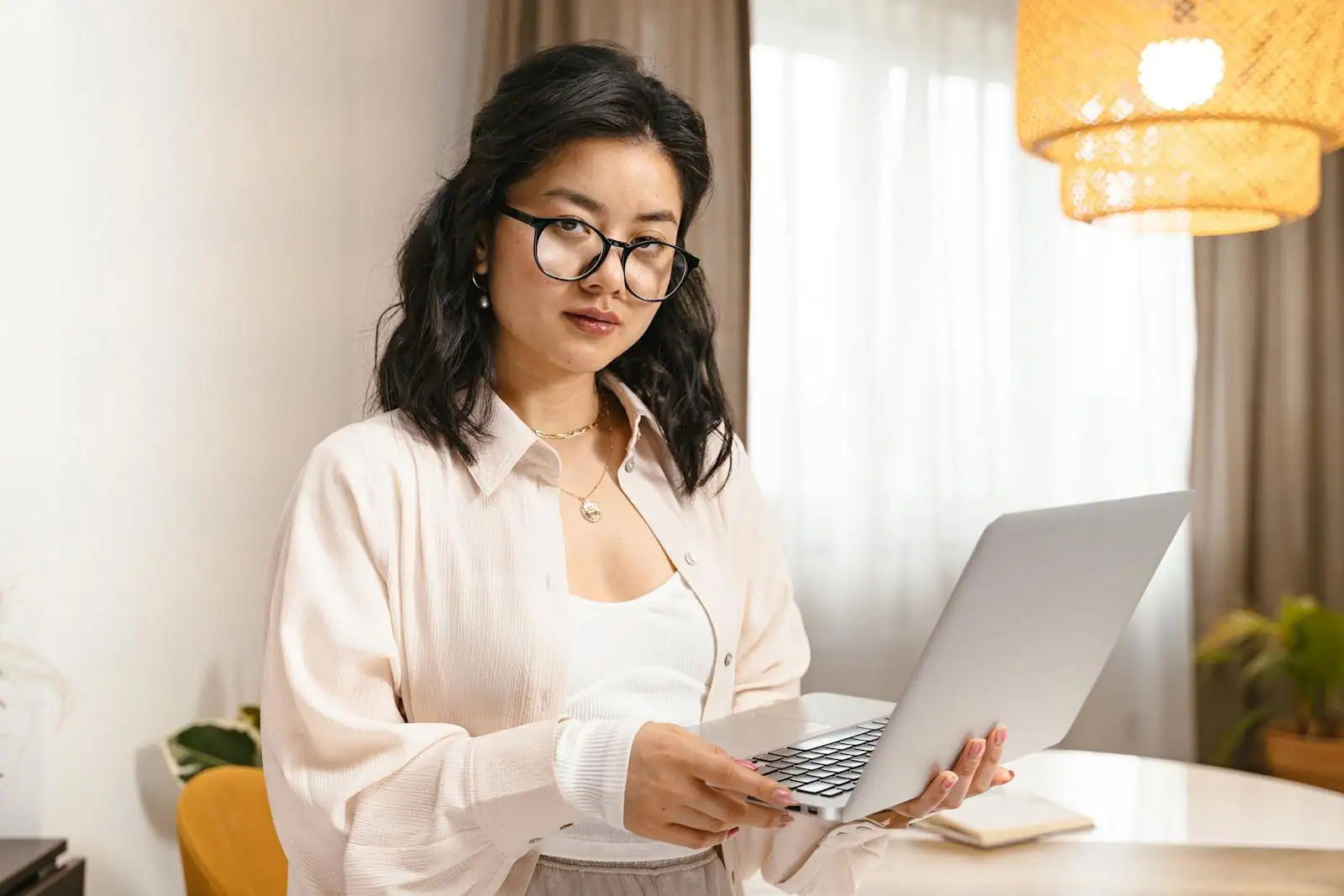 Une jeune femme à lunettes tient un ordinateur portable dans un intérieur lumineux