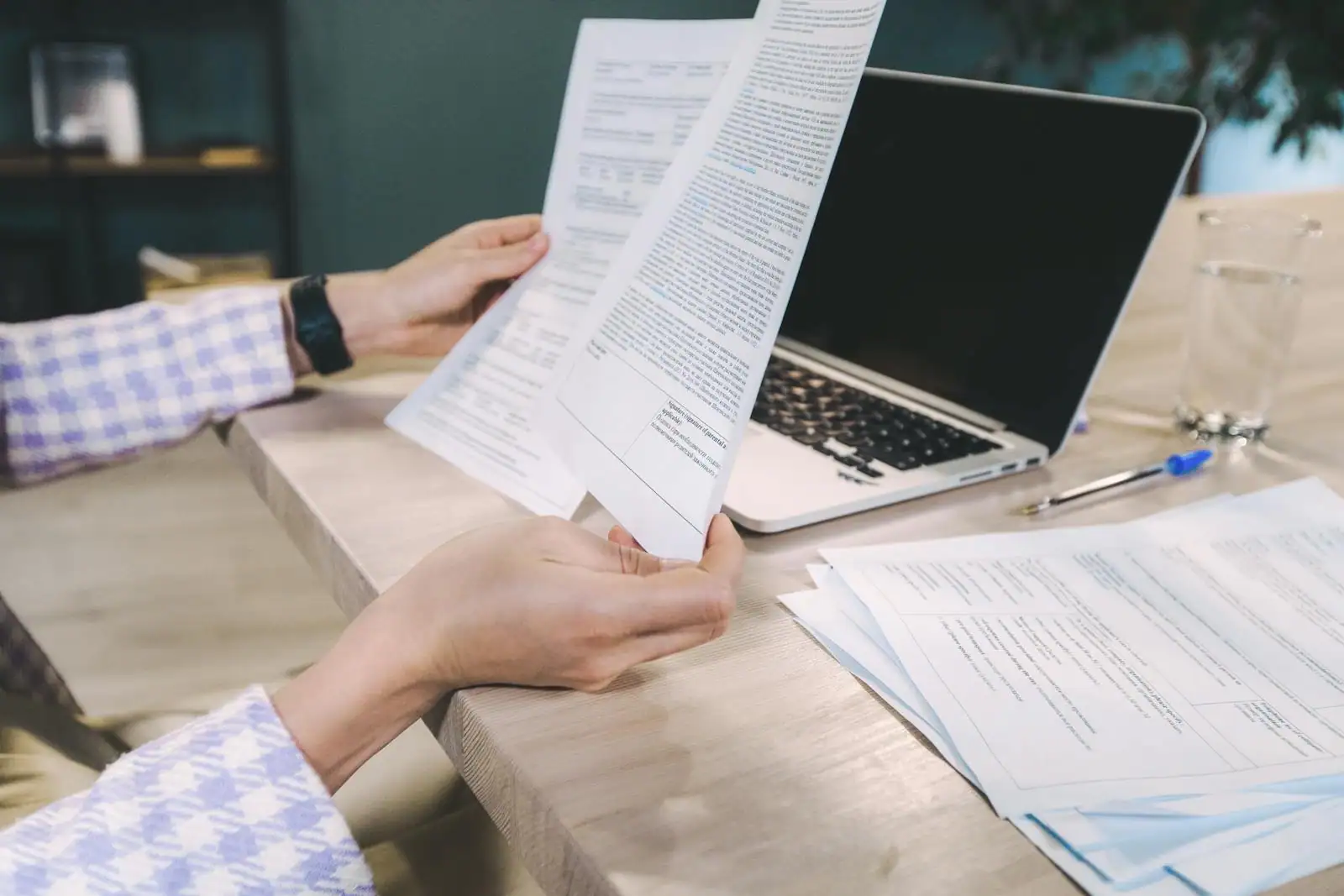 Personne lisant des documents imprimés à un bureau, à côté d'un ordinateur portable.