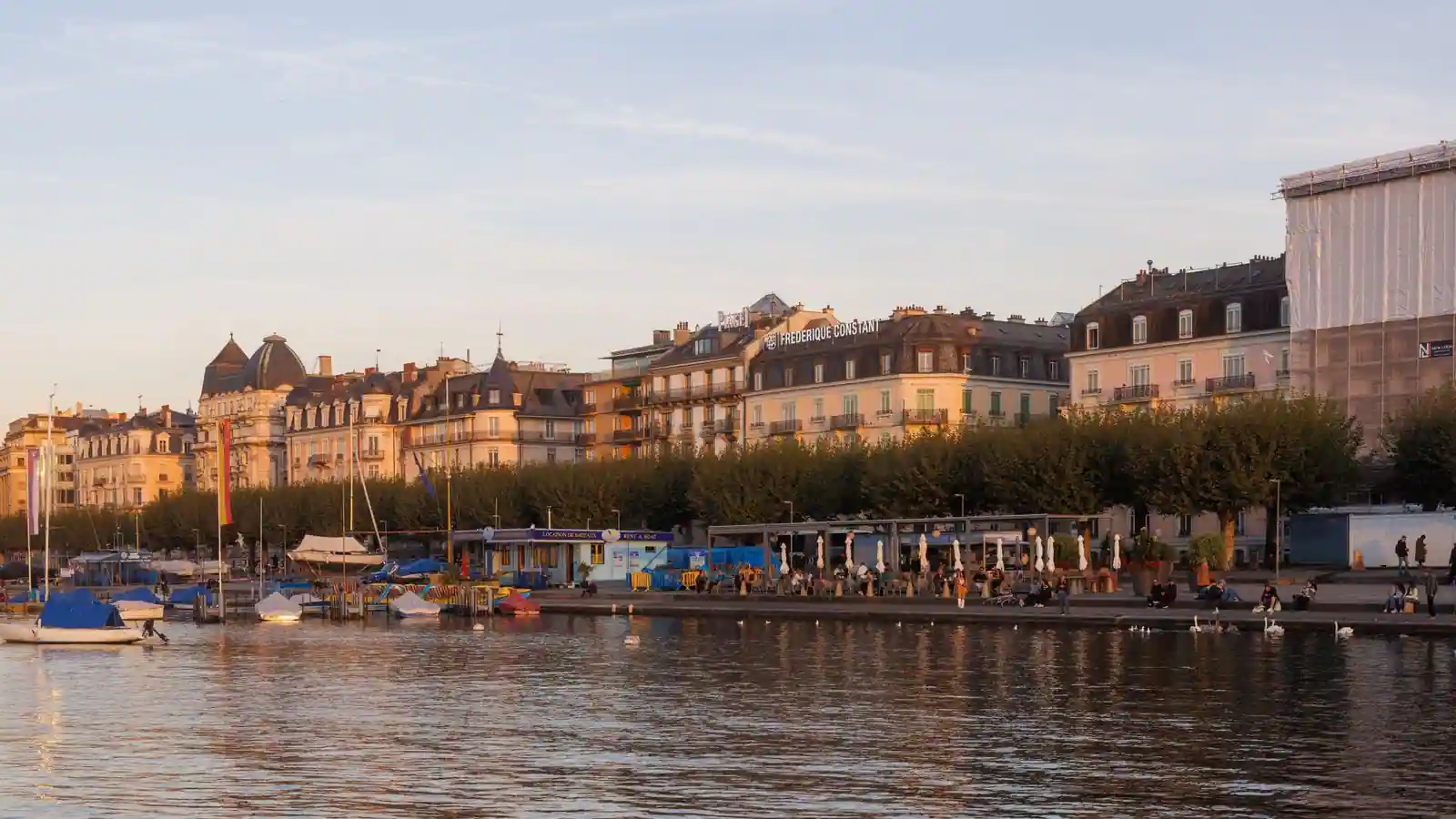 Le bord du lac à Genève, en Suisse, au coucher du soleil, avec les immeubles du quai et des bateaux