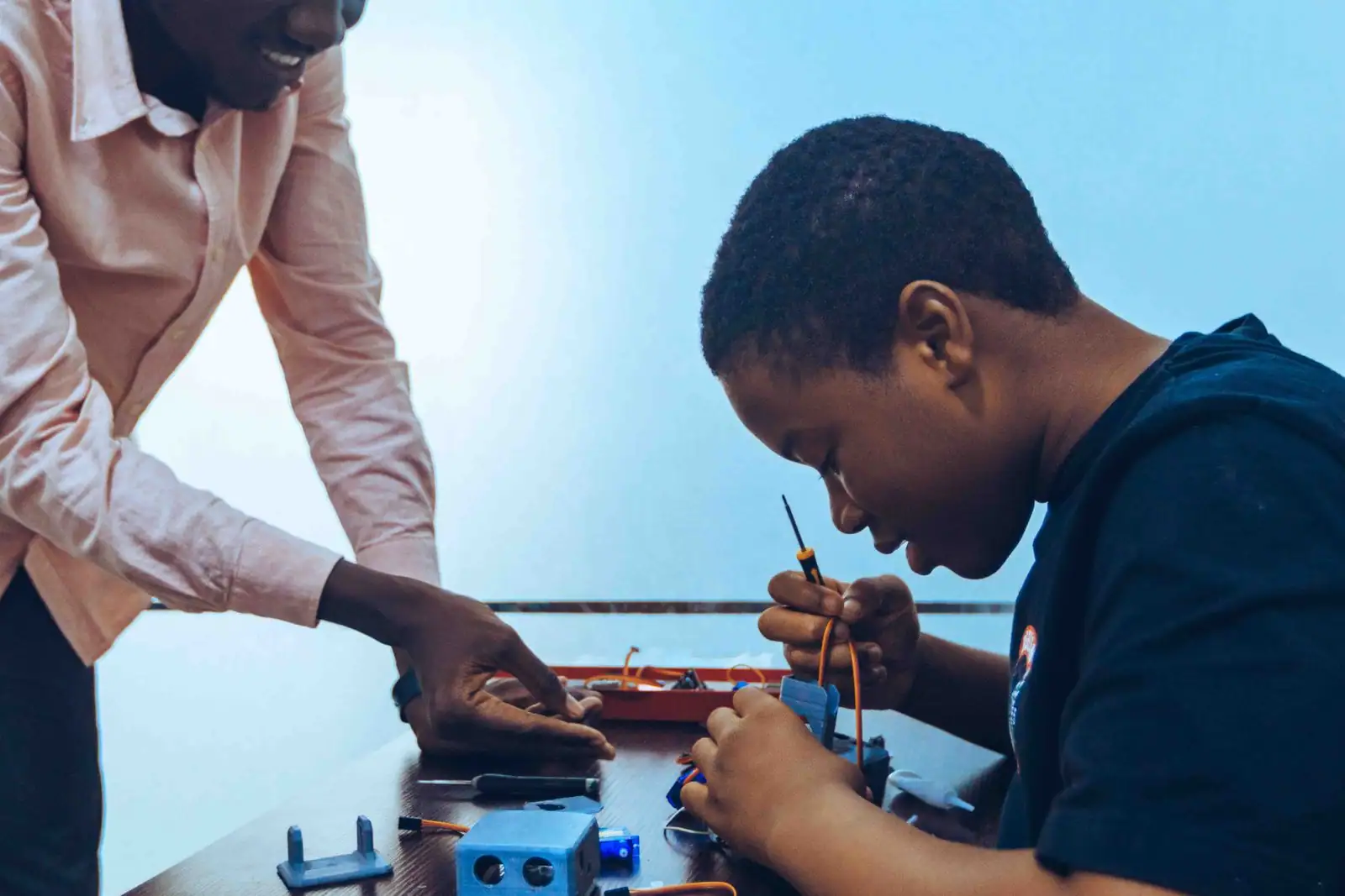 Jeune apprenant concentré sur un montage électronique, guidé par un formateur en atelier