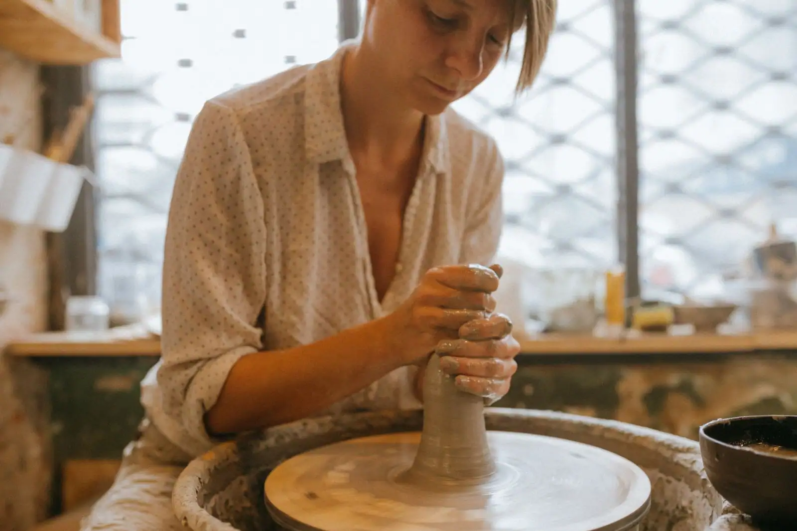 Femme concentrée façonnant de l'argile sur un tour de potier dans un atelier lumineux