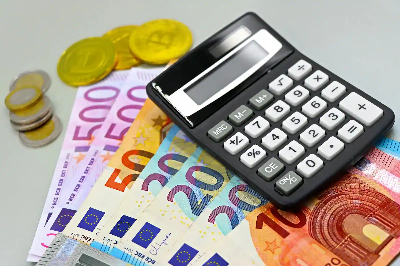 Billets et pièces en euros posés à côté d'une calculatrice sur un bureau, évoquant le budget et la fiscalité