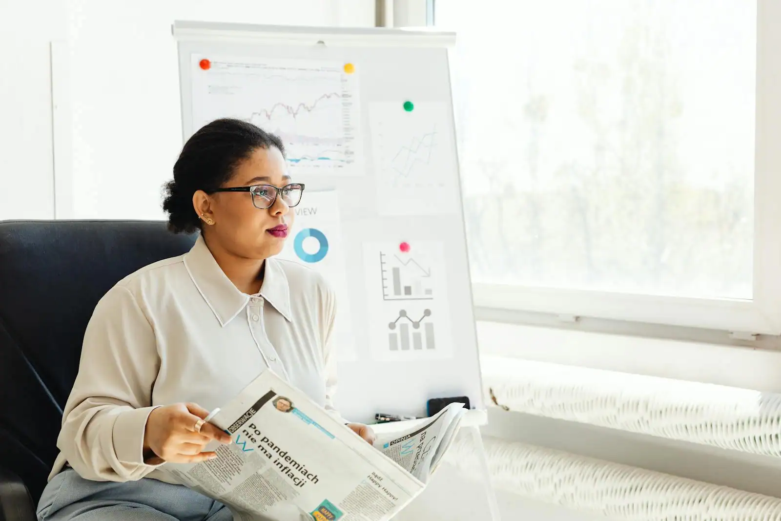 Une femme dans un bureau tient un journal devant un tableau de graphiques économiques