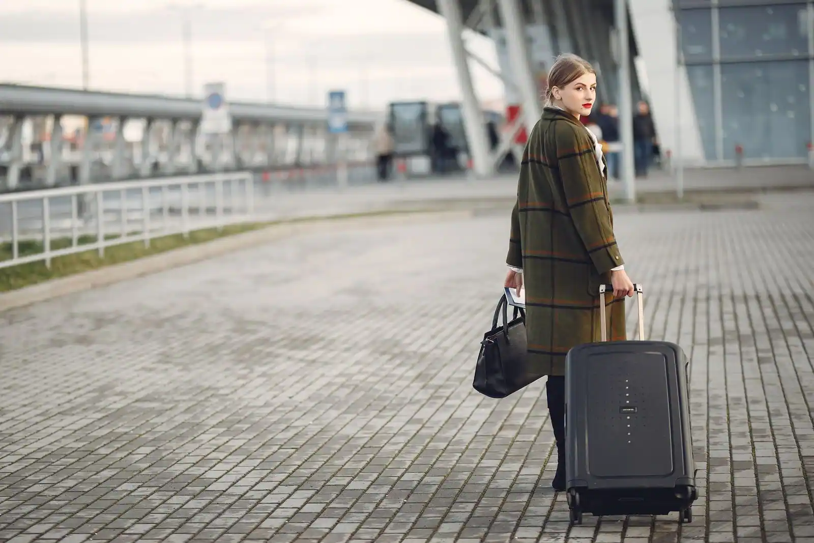 Voyageuse tirant sa valise devant le terminal d'un aéroport, billet en main avant l'embarquement de son vol
