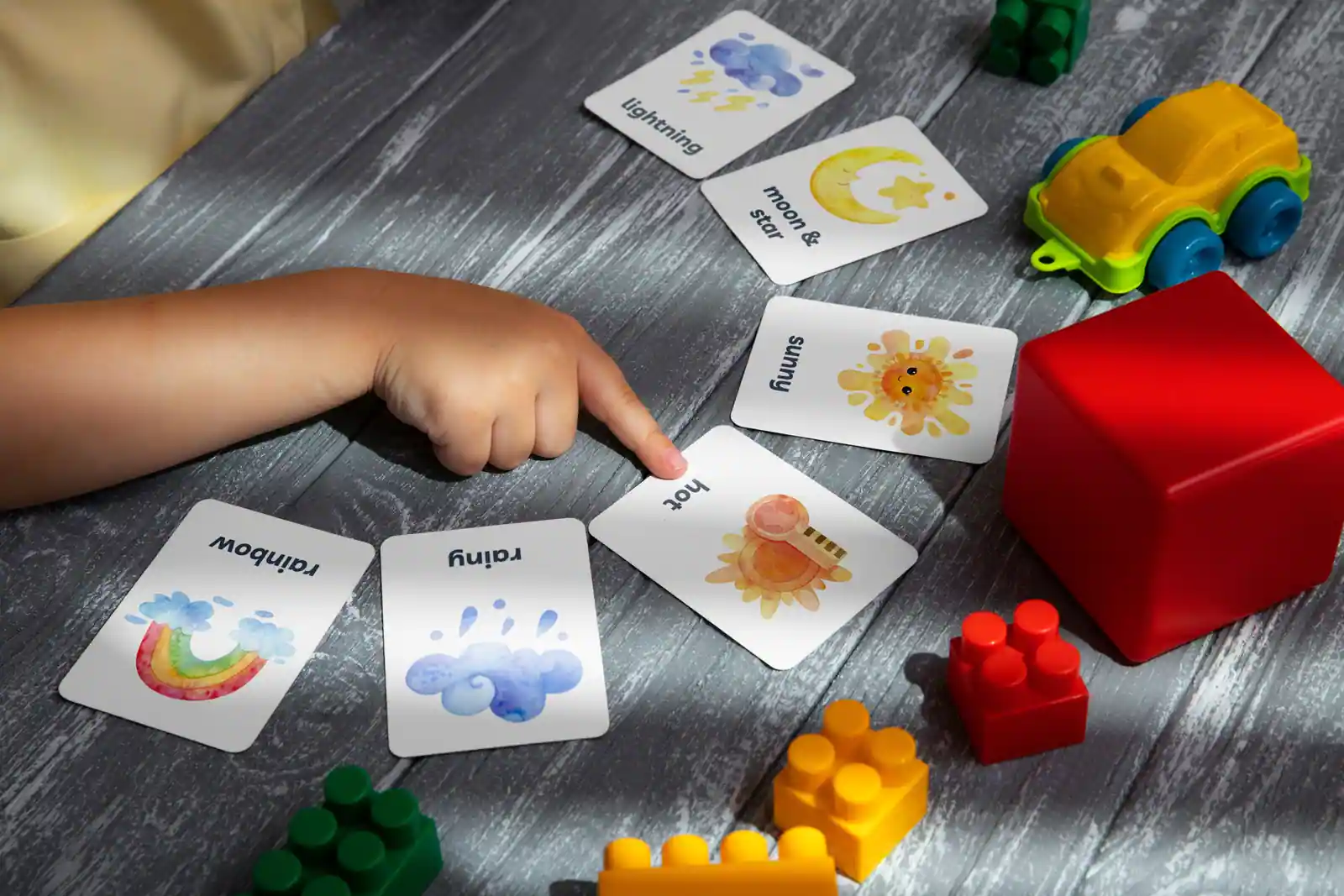 Main d’enfant désignant une carte illustrée parmi d’autres, le geste au cœur de la communication par images.