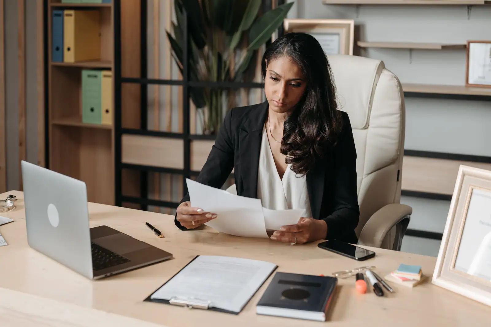 Professionnelle lisant des documents à son bureau, ordinateur portable ouvert devant elle