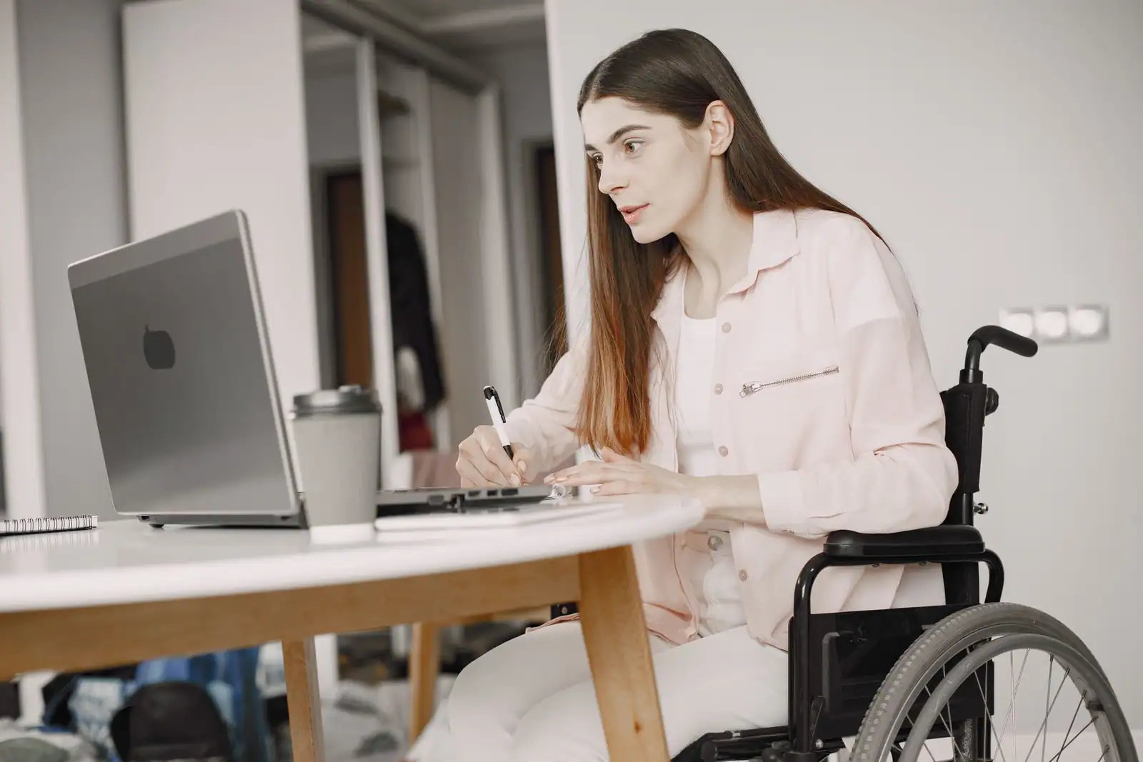 Jeune femme en fauteuil roulant prenant des notes stylo en main devant son ordinateur portable