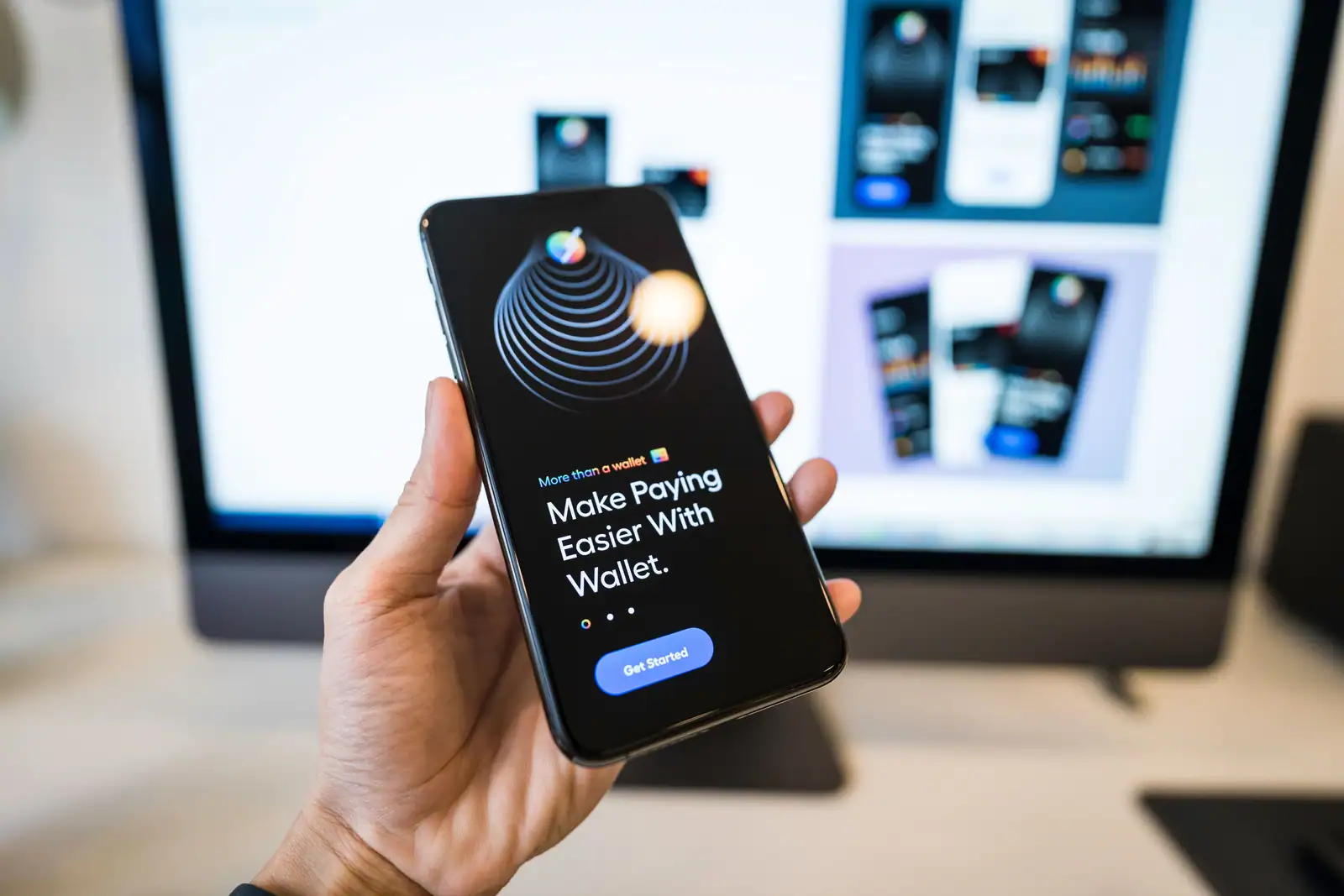 Main tenant un smartphone affichant une application de paiement mobile, écran d'ordinateur en arrière-plan