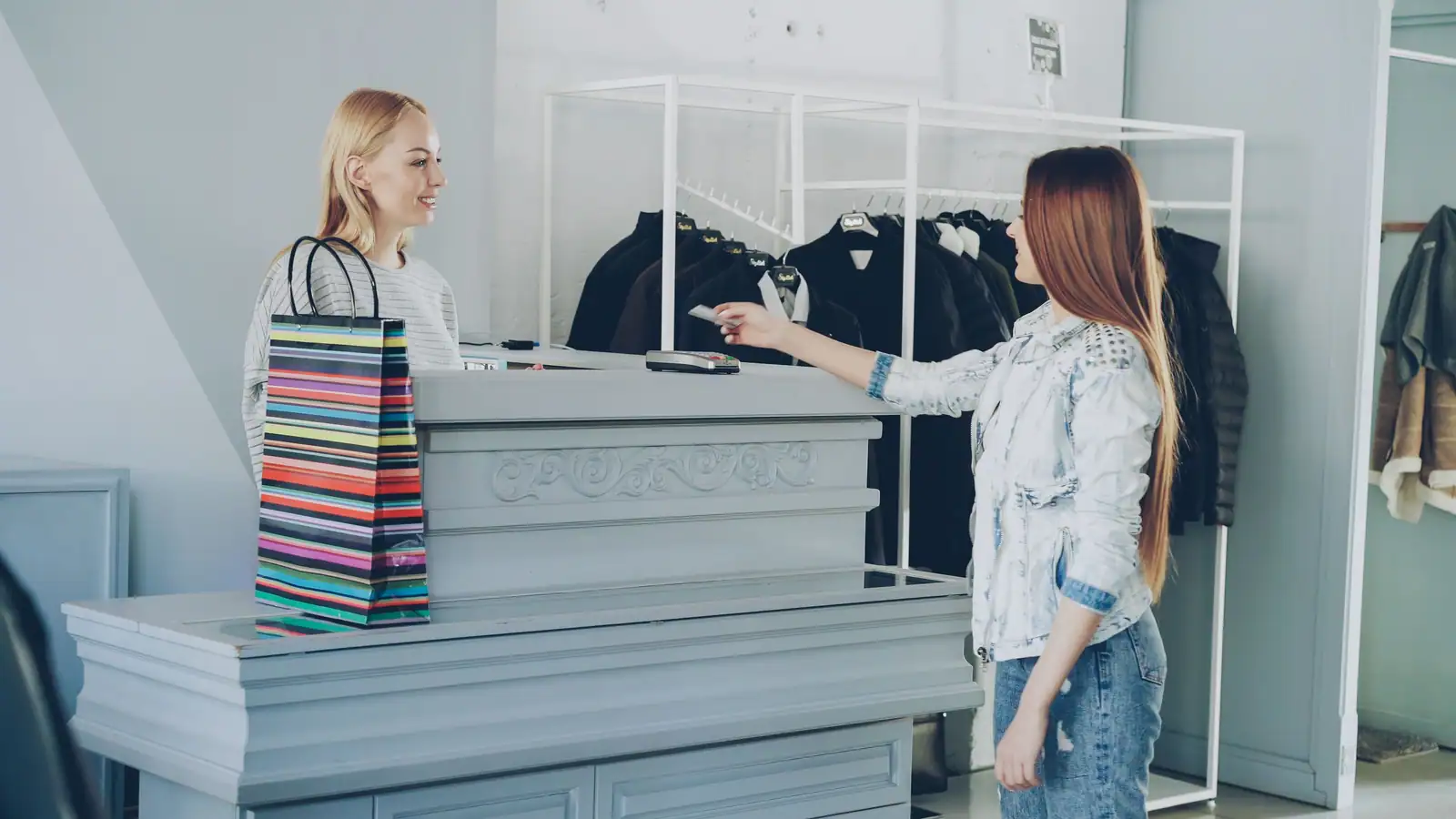 Cliente tendant une carte à la vendeuse au comptoir d’une boutique de vêtements.