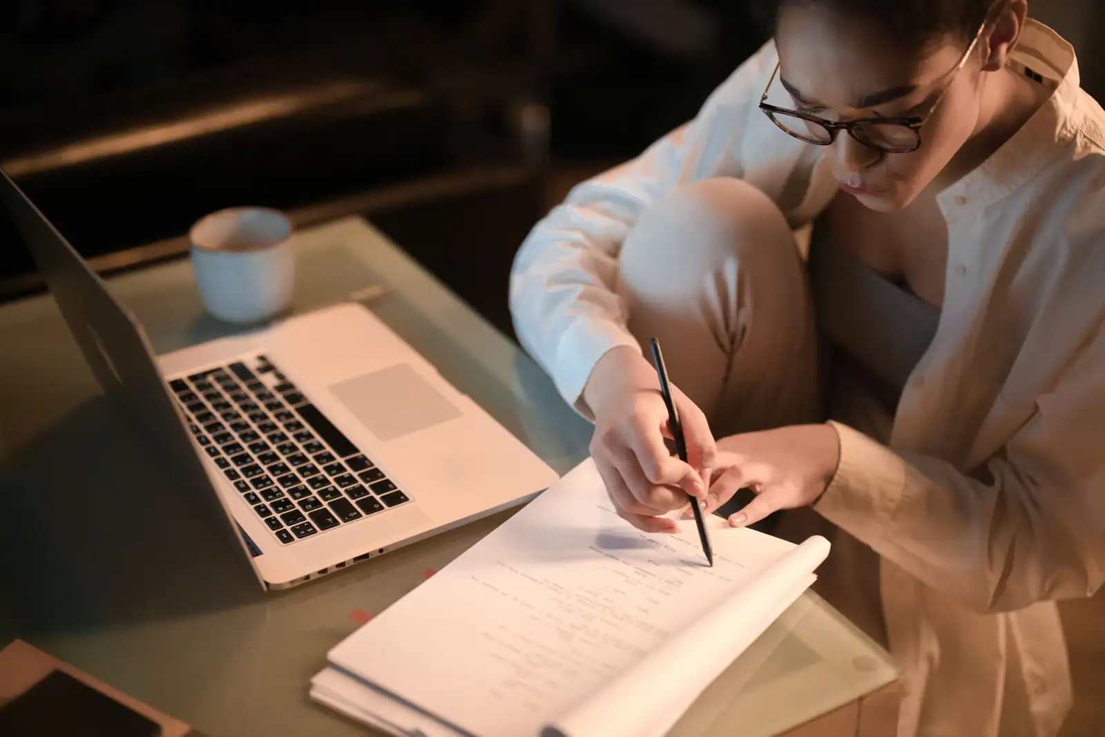 Femme étudiant le soir, annotant des documents de formation près d’un ordinateur portable