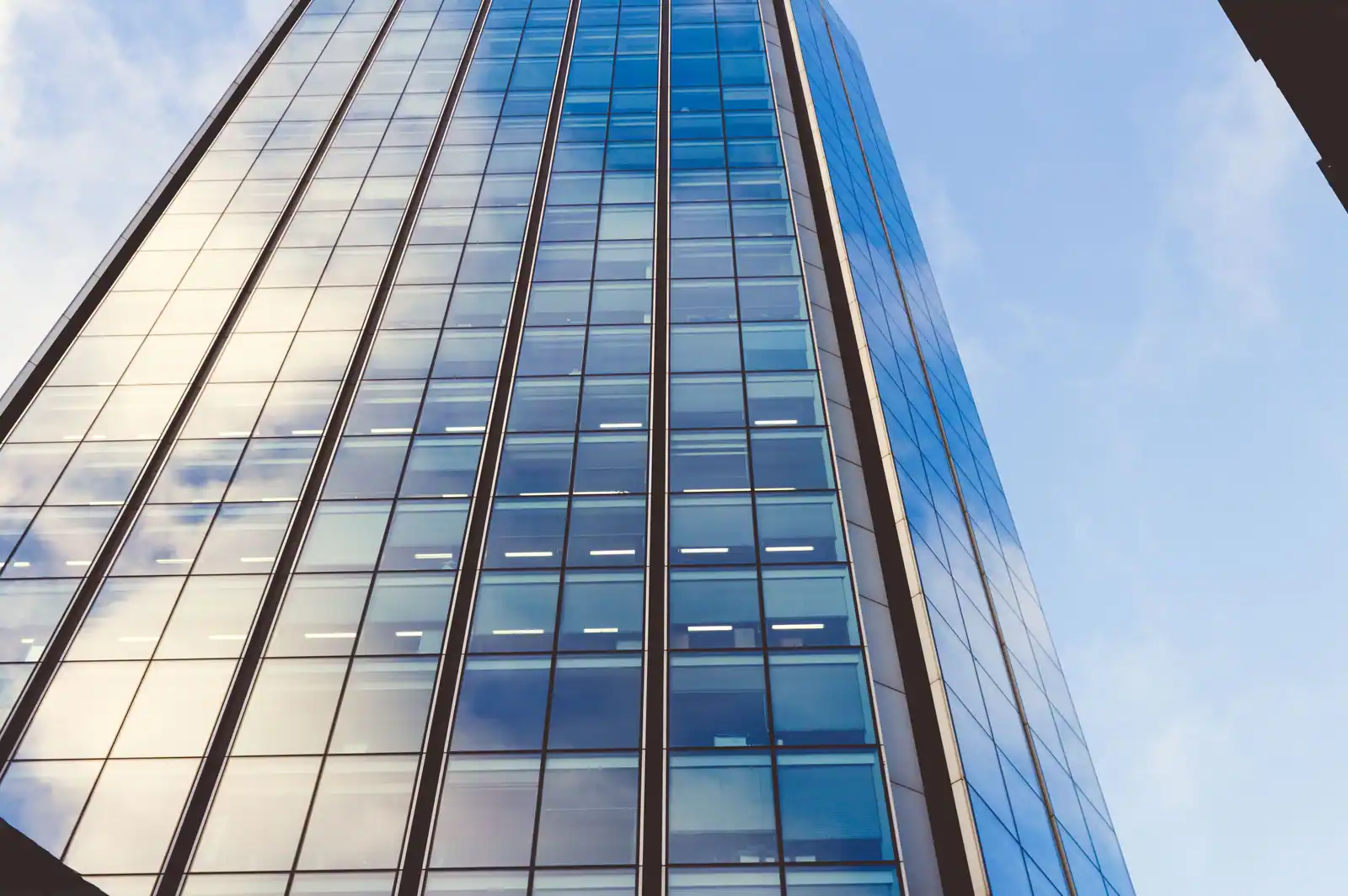 Tour de bureaux vitrée dans un quartier d'affaires, façade financière anonyme et sobre.