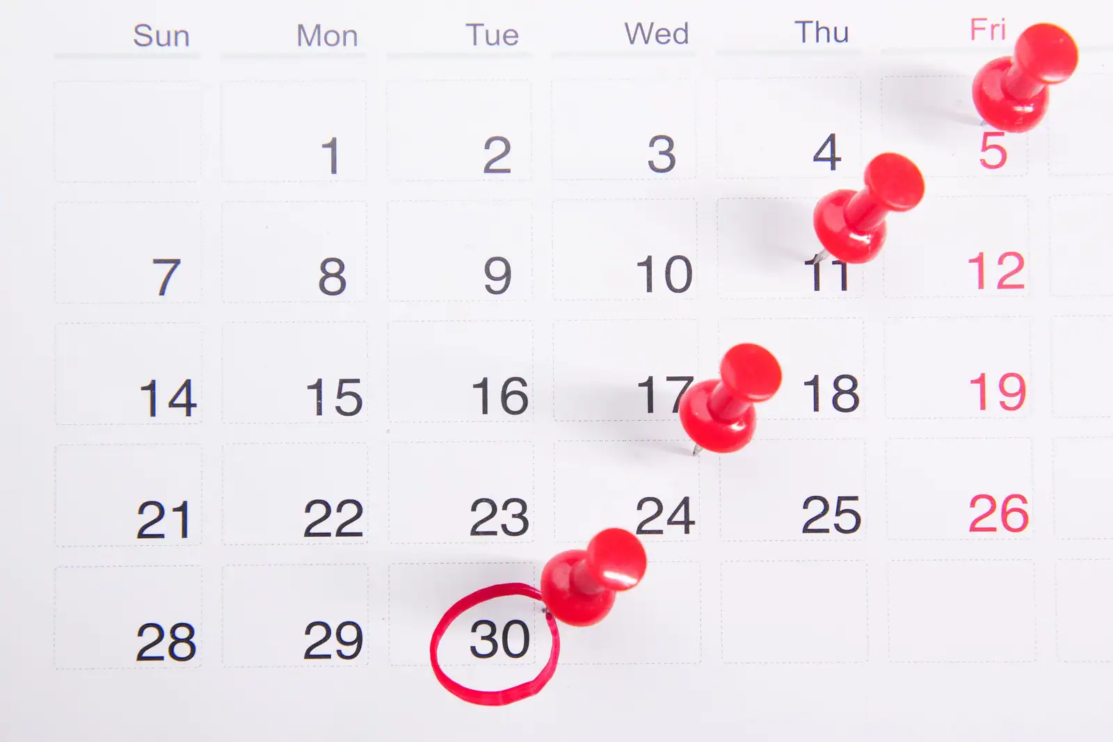 Calendrier mural avec des dates marquées par des punaises rouges et une date entourée en rouge.