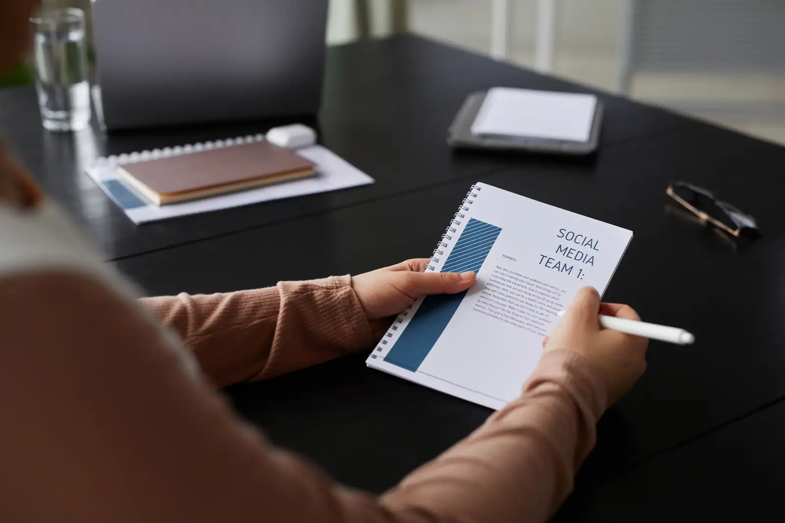 Femme tenant un carnet marqué social media team dans un bureau, avec ordinateur et tablette