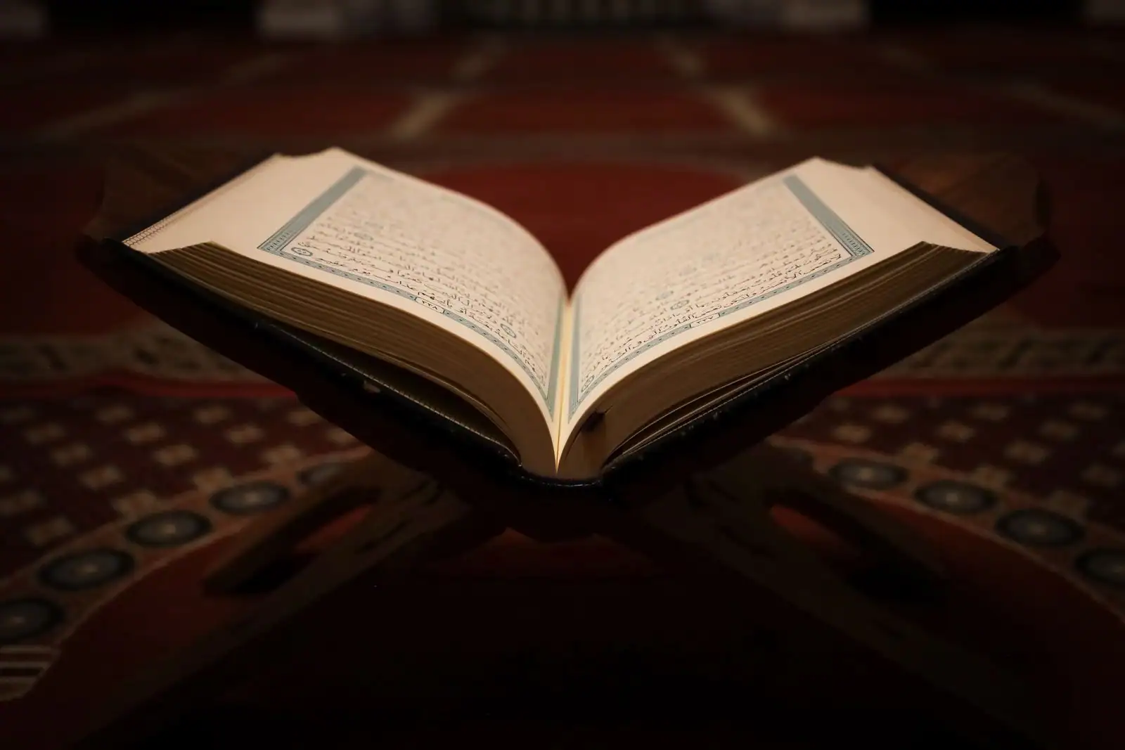Coran ouvert posé sur un support en bois dans une mosquée, pages visibles, ambiance calme et recueillie.