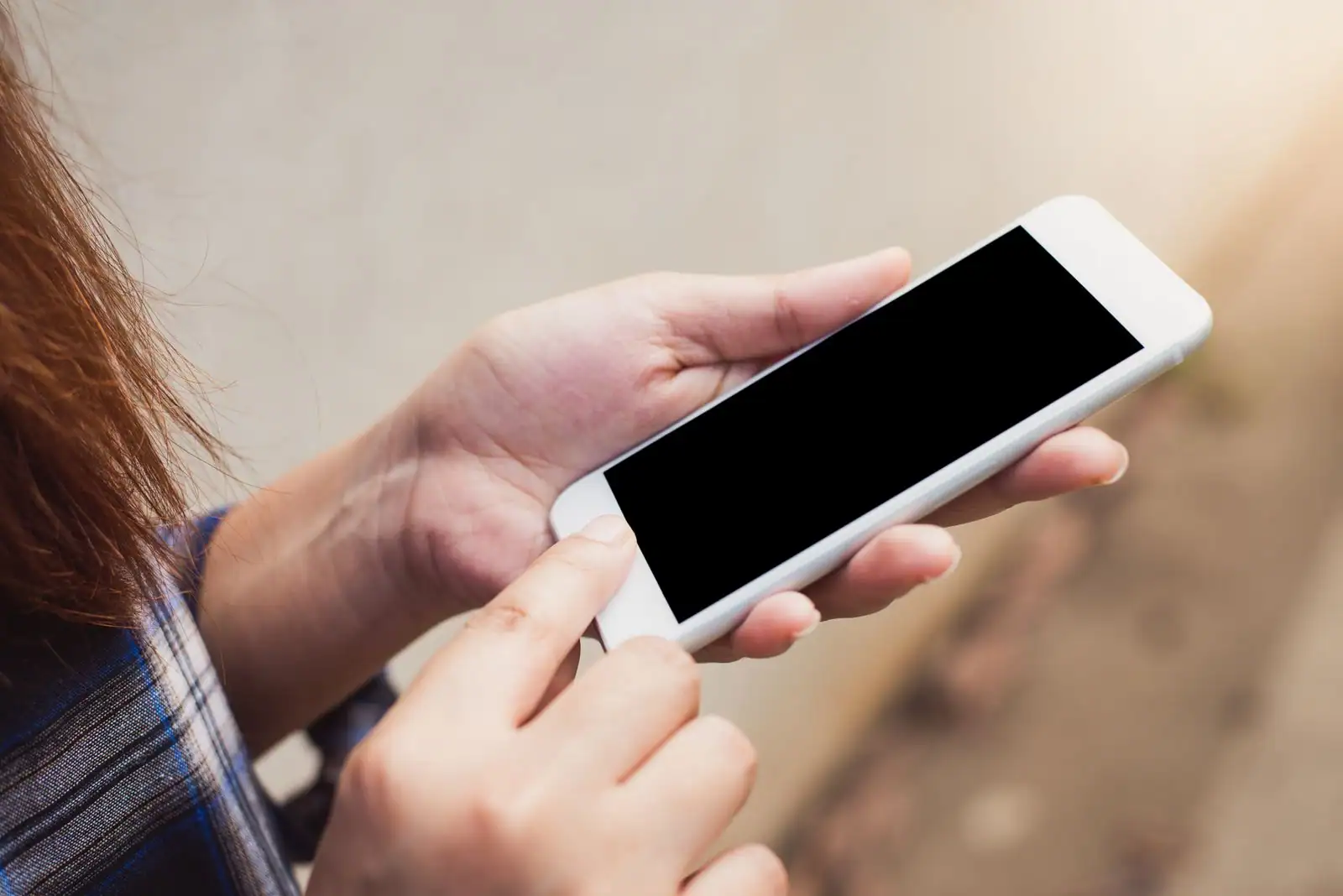 Personne tenant à deux mains un smartphone à l'écran noir, geste de connexion à une application mobile