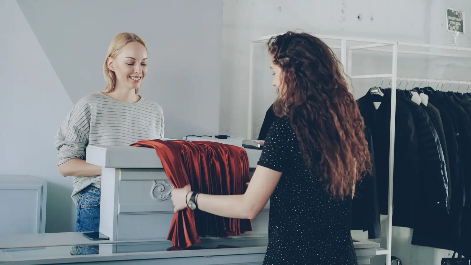 Une vendeuse aide une cliente à choisir un vêtement, échange au comptoir d'une boutique.
